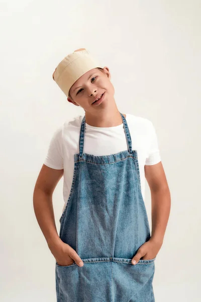 Niño discapacitado con síndrome de Down vestido como cocinero en delantal y sombrero sonriendo a la cámara mientras posa aislado sobre fondo blanco —  Fotos de Stock