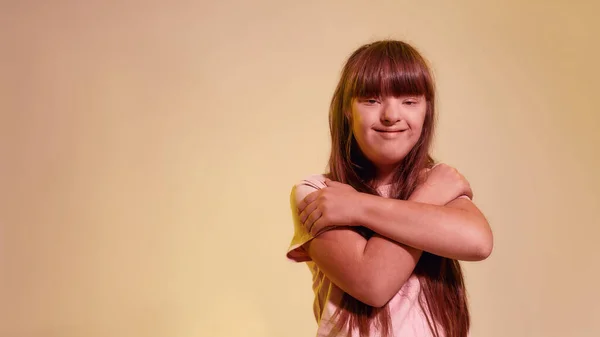 Retrato de una chica discapacitada con síndrome de Down sonriendo a la cámara, de pie con los brazos cruzados mientras posa aislada sobre un fondo amarillo creativo — Foto de Stock