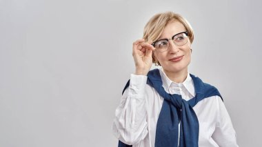 Zarif orta yaşlı beyaz kadın portresi iş elbisesi giyiyor, gözlüklerini ayarlıyor, gülümsüyor ve gri arka planda tek başına duruyor.