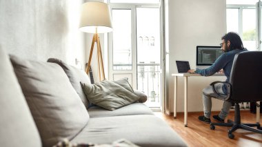 Merkez ofis. Genç adamın arka görünüşü, yazılım geliştiricisi iş yerinde otururken bilgisayarına kod yazıyor ve evden çalışıyor.