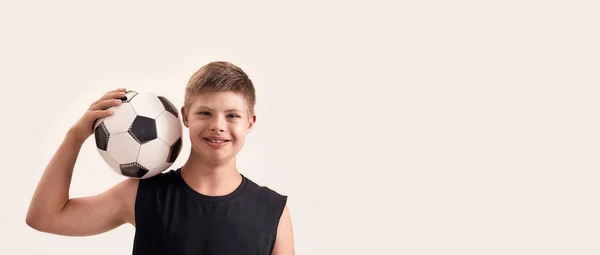 Joyeux garçon handicapé avec le syndrome de Down souriant à la caméra tout en posant avec le football isolé sur fond blanc — Photo