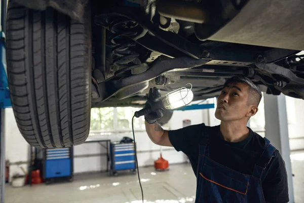 Mecánico asiático examinando auto parte inferior con linterna — Foto de Stock