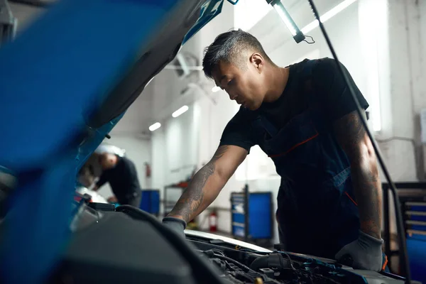 Młody azjatycki mechanik pracujący z silnikiem przy otwartym kapturze — Zdjęcie stockowe