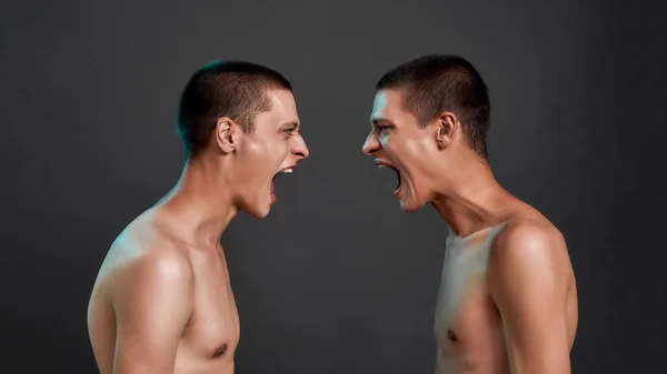 Dos jóvenes medio desnudos enojados hermanos gemelos caucásicos discutiendo, gritando mientras están de pie cara a cara aislados sobre fondo gris oscuro —  Fotos de Stock