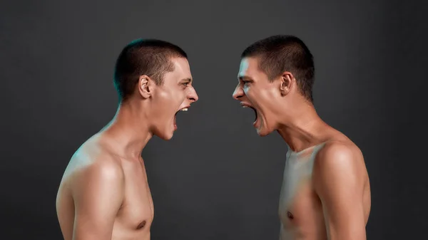 Twee jonge halfnaakte blanke tweelingbroers ruziënd, schreeuwend terwijl ze oog in oog stonden geïsoleerd over donkergrijze achtergrond — Stockfoto