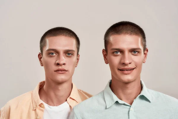 Sorgsenhet och lycka. Närbild porträtt av två unga kaukasiska tvillingbröder tittar på kamera med olika ansiktsuttryck samtidigt står isolerade över beige bakgrund — Stockfoto