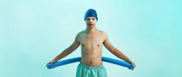 障害児ダウン症候群の水泳キャップのカメラを見て、泡麺を保持しながら、ターコイズの背景に孤立ポーズ。水泳リハビリテーションの概念 — ストック写真