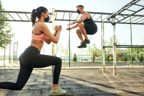 Erkek şehir spor sahasında zıplarken kız çömeliyor.