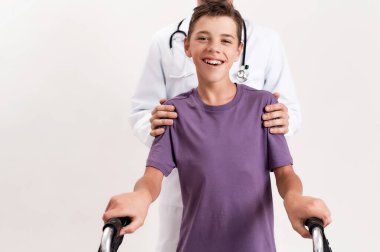 Serebral felçli engelli bir çocuğa yardım eden erkek doktor, beyaz arka planda izole edilmiş yürütecini kullanarak adımlar atıyor.