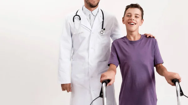 Cropped shot of male doctor helping teenaged disabled boy with cerebral palsy, taking steps using his walker isolated over white background — Stock Fotó