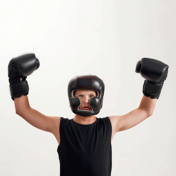 Niño discapacitado con síndrome de Down con guantes de boxeo y casco, mirando a la cámara, levantando los brazos, sintiéndose fuerte mientras posa aislado sobre fondo blanco — Foto de Stock