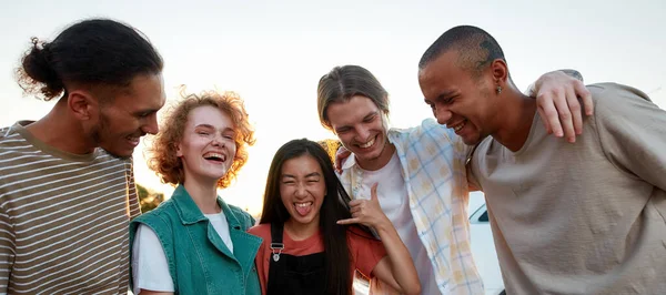 Пять случайно одетых друзей разных национальностей хорошо проводят время на улице, смеясь и улыбаясь обнимаясь. — стоковое фото