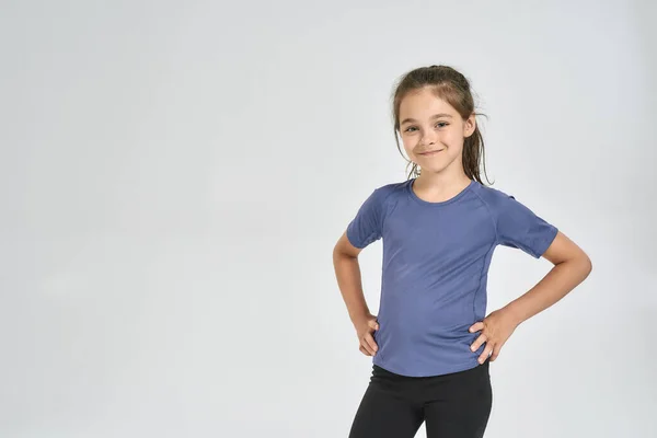 Kis sportos lány gyermek sportruházat mosolyog a kamera, miközben áll elszigetelt fehér háttér — Stock Fotó