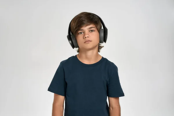Liten sportig pojke barn i sportkläder bär hörlurar, lyssna på musik, titta på kameran medan poserar isolerad över vit bakgrund — Stockfoto