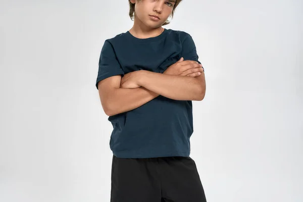 Обрезанный снимок маленького спортивного мальчика в спортивной одежде, позирующего, стоя со скрещенными руками на белом фоне — стоковое фото