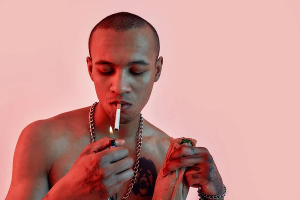 Sigara ve içki. Ağzında sigara yakan dövmeleri olan koyu tenli üstsüz bir adam. — Stok fotoğraf
