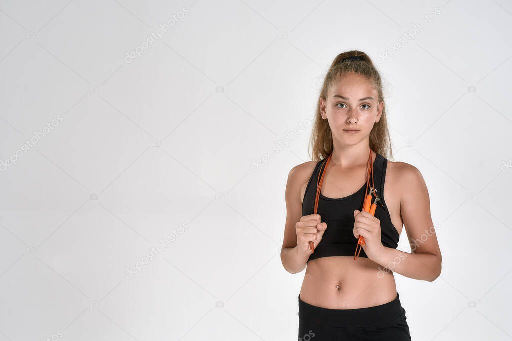 Portrait of cute sportive girl child in black sportswear looking at camera, standing with jump rope while posing isolated over white background