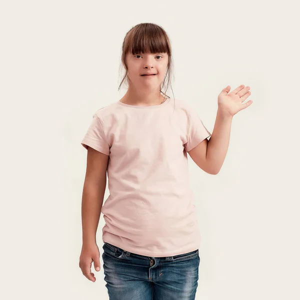 Retrato de menina com deficiência com síndrome de Down sorrindo enquanto acena para a câmera, em pé isolado sobre fundo branco — Fotografia de Stock