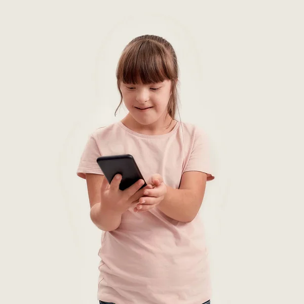 Retrato de chica discapacitada con síndrome de Down sosteniendo teléfono inteligente, mirando a la pantalla mientras posa aislado sobre fondo blanco —  Fotos de Stock