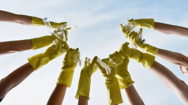 Rädda vår planet. Grupp frivilliga eller miljöaktivister bär gula skyddshandskar gummi som håller plastflaskor mot blå himmel — Stockfoto