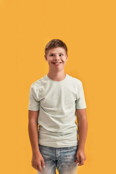 Potret anak remaja yang periang dan cacat dengan sindrom Down tersenyum pada kamera sambil berdiri terisolasi di atas latar belakang kuning — Stok Foto