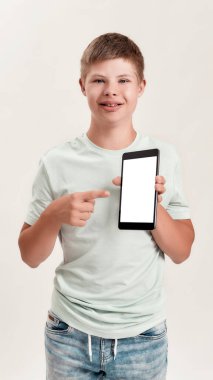 Down sendromlu mutlu çocuk gülümsüyor, beyaz arka planda tek başına dururken boş ekranla tablet bilgisayarına bakıyor ve işaret ediyor.