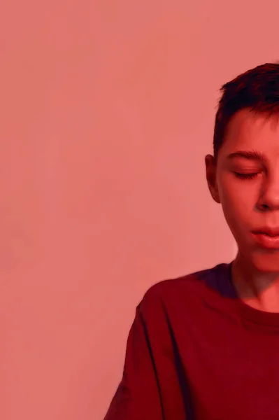 Cropped portrait of teenaged disabled boy with cerebral palsy keeping his eyes closed, looking thoughtful while posing isolated over red light background — Stock Fotó