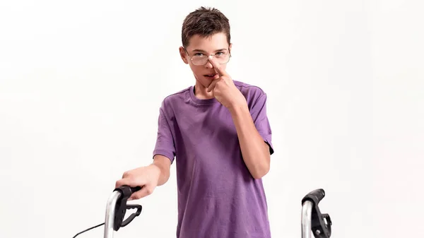 Niño discapacitado adolescente con parálisis cerebral mirando a la cámara, ajustando las gafas mientras toma medidas con su andador aislado sobre fondo blanco — Foto de Stock