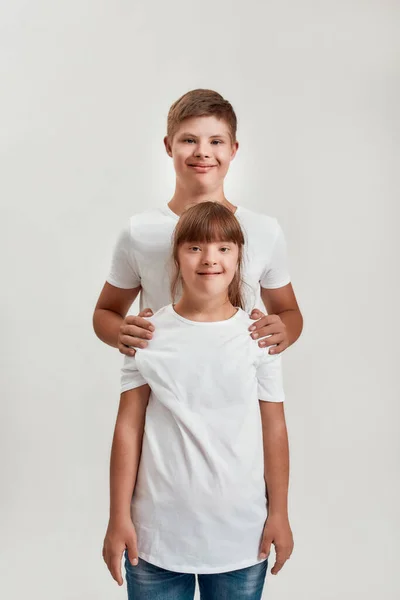 Duas crianças, menino e menina com deficiência com síndrome de Down sorrindo para a câmera enquanto posando juntos isolado sobre fundo branco — Fotografia de Stock