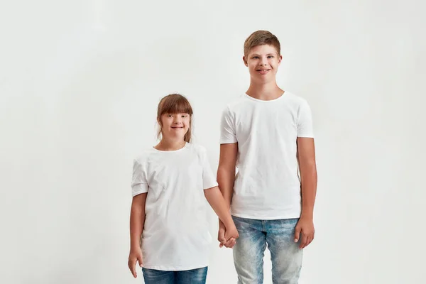 Duas crianças, menino e menina com deficiência com síndrome de Down sorrindo para a câmera, segurando as mãos um do outro enquanto posando juntos isolado sobre fundo branco — Fotografia de Stock