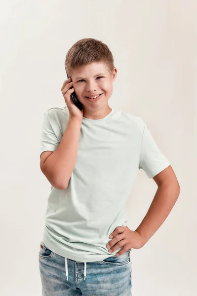 Retrato de un adolescente discapacitado con síndrome de Down sonriendo a la cámara mientras habla por teléfono, parado aislado sobre fondo blanco — Foto de Stock
