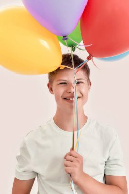 Down sendromlu mutlu, engelli bir gencin portresi kameraya gülümsüyor, bir sürü renkli balon tutuyor ve beyaz arka planda tek başına duruyor.
