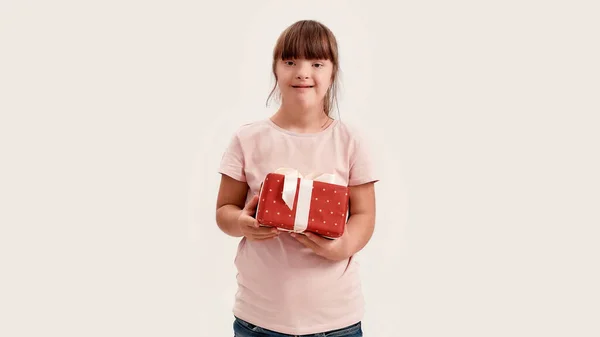 Retrato de chica discapacitada con síndrome de Down sonriendo a la cámara, sosteniendo regalo de cumpleaños mientras posando aislado sobre fondo blanco —  Fotos de Stock