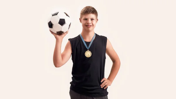 Joyful disabled boy with Down syndrome wearing gold medal smiling at camera while posing with football isolated over white background — Stock Photo, Image