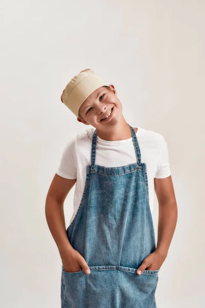 Niño discapacitado con síndrome de Down vestido como cocinero en delantal y sombrero sonriendo a la cámara mientras posa aislado sobre fondo blanco — Foto de Stock