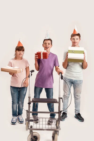 Full length shot of three disabled children wearing birthday caps smiling at camera and holding presents while celebrating birthday together isolated over white background — Stock Photo, Image