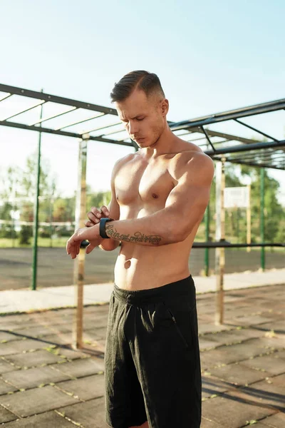 Aktif genç yarı çıplak adam dışarıda spor yaparken akıllı saatini kullanarak sonuçları kontrol ediyor.