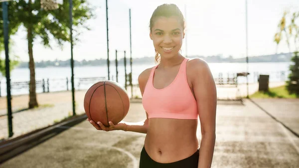 Güneşli bir günde dışarıda basketbol oynarken kameraya gülümseyen mutlu genç kız. — Stok fotoğraf