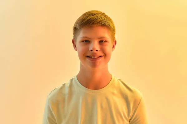 Portrait of joyful disabled boy with Down syndrome smiling at camera while posing isolated over yellow light background — Stok Foto