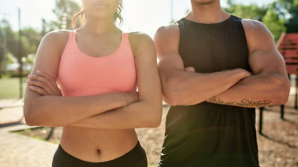 Przycięty strzał sportowej młodej pary, mężczyzna i kobieta stojący z ramionami skrzyżowane podczas treningu razem na siłowni na świeżym powietrzu — Zdjęcie stockowe