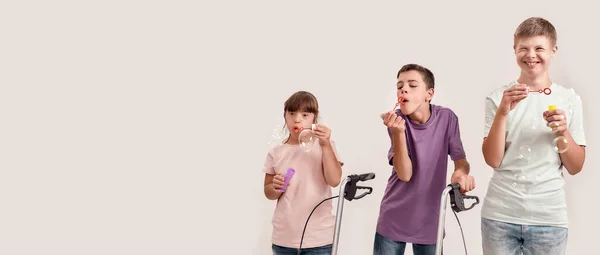 Three cheerful disabled children with Down syndrome and cerebral palsy smiling while blowing soap bubbles, standing together isolated over white background — Stock Photo, Image