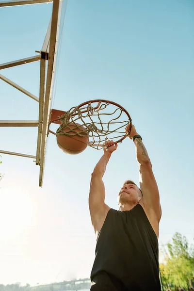 Skilled sportive guy throwing ball into basket, while playing basketball outdoors — Stok Foto
