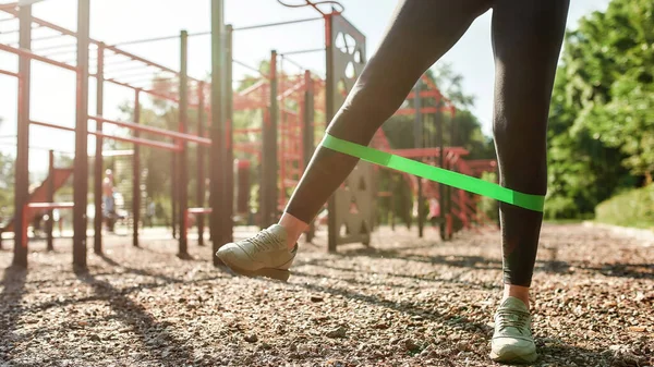Närbild av ben ung kvinna träning med elastiskt band på utomhus gym på en solig dag — Stockfoto