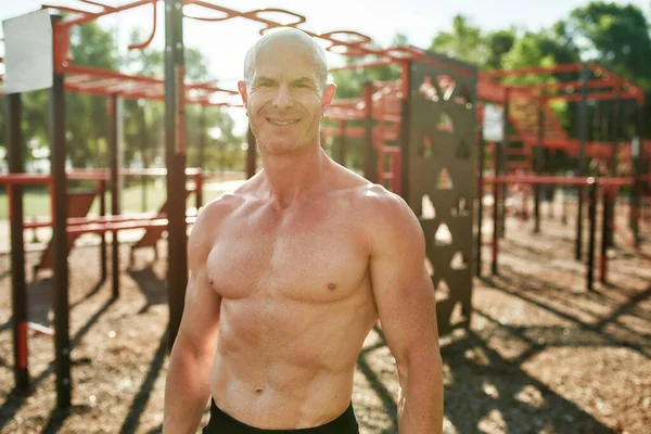 Mature male boxer with naked torso smiling at camera, standing outdoors while having workout at street gym yard — Stok Foto