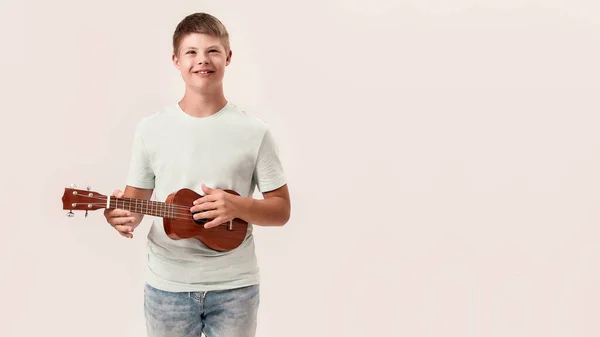 Веселий хлопчик з інвалідністю з синдромом Дауна посміхається, граючи в укулеле, стоїть ізольовано на білому тлі — стокове фото
