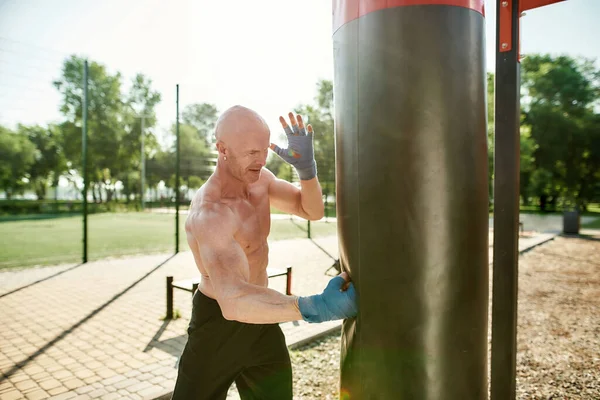 Athletic mature male boxer training, using punching bag, having workout at street gym yard — Fotografia de Stock