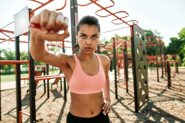 Portrait of concentrated young mixed race sportive woman having workout with rubber band at street gym yard — Fotografia de Stock