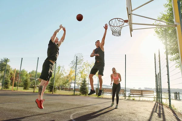 Athletic young friends spending time together outdoors on playground, playing basketball on a sunny day — Stok Foto