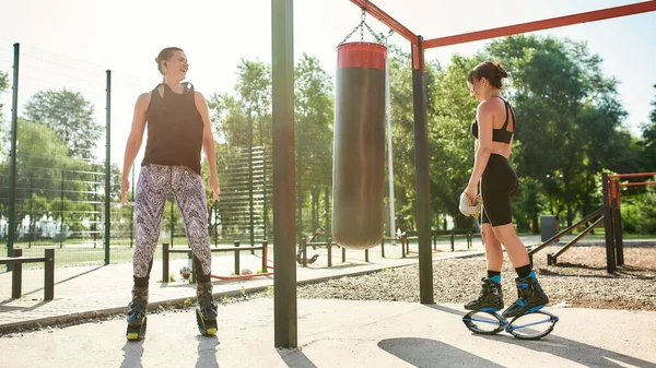 Colpo completo di due donne sportive in scarpe da salto kangoo allenamento con sacco da boxe, avendo allenamento in cortile palestra di strada — Foto Stock