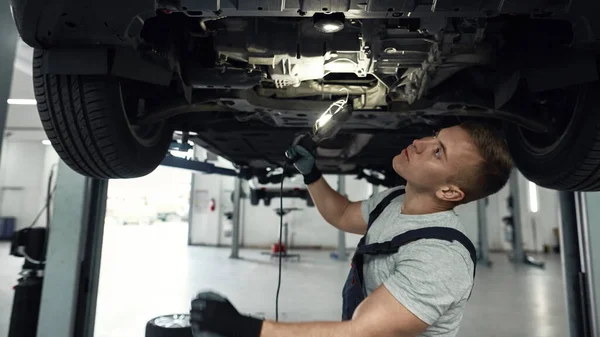 Mecánico caucásico examinando fondo de la máquina usando linterna — Foto de Stock